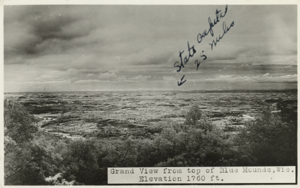 Photographic postcard of the view towards Madison from the top of Blue Mounds. Handwritten on the card is "State Capitol, 25 miles" with an arrow. Text below reads "Grand View From top of Blue Mounds, Wis. Elevation 1760 ft."