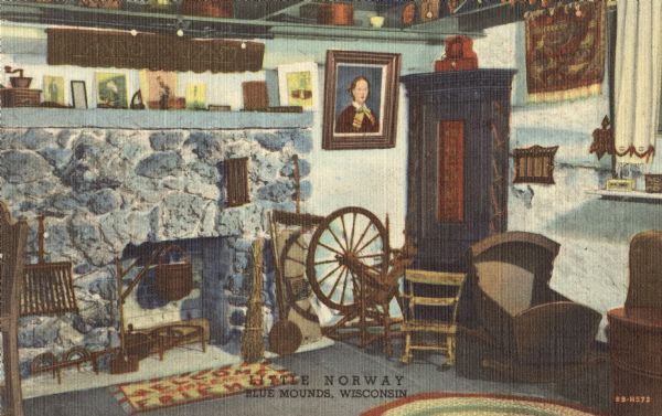Colorized postcard of the main living area of a Norwegian dwelling at Little Norway showing a fireplace, cradle and spinning wheel. Pictures and household objects line the mantlepiece. Text below reads: "Little Norway, Blue Mounds, Wisconsin."