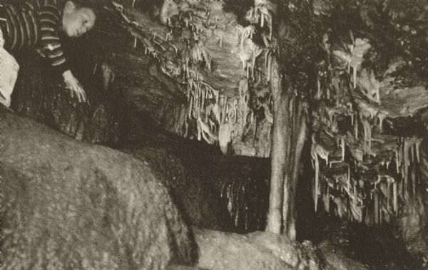 Postcard of a boy peering at stalactites and cave onyx terraces on the Enchanted Mountain in the Cave of the Mounds.