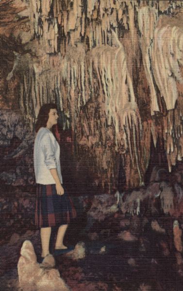 Colorized postcard of a woman viewing stalactites in the Chapel, North Cave, in the Cave of the Mounds.