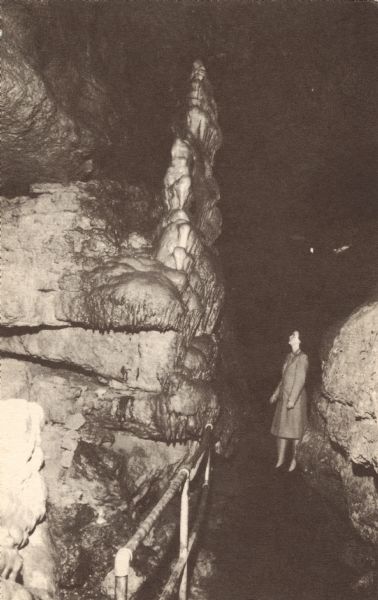 Colorized postcard of the Hall of Statuary in the South Section at the Cave of the Mounds. A woman is gazing up at the formation.