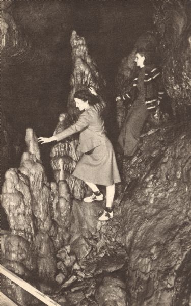 Photographic postcard of two women climbing on stalagmites in the Cave of the Mounds.