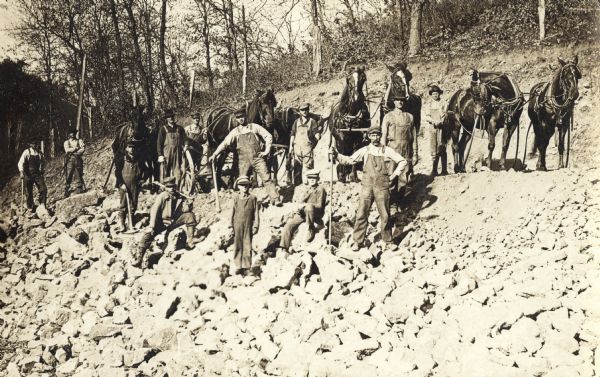 Photographic postcard of workmen and young boys posing with horses and hand tools. They are working on an excavating project near Boscobel.