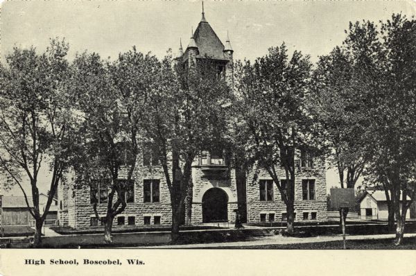 Photographic postcard of Boscobel High School seen through the trees. Text below reads: "High School, Boscobel, Wis."