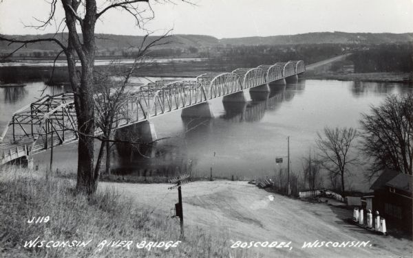 Photographic postcard from hill looking down at the bridge over the Wisconsin River. A gas station is visible on the right. Text below reads: "Wisconsin River Bridge, Boscobel, Wisconsin."