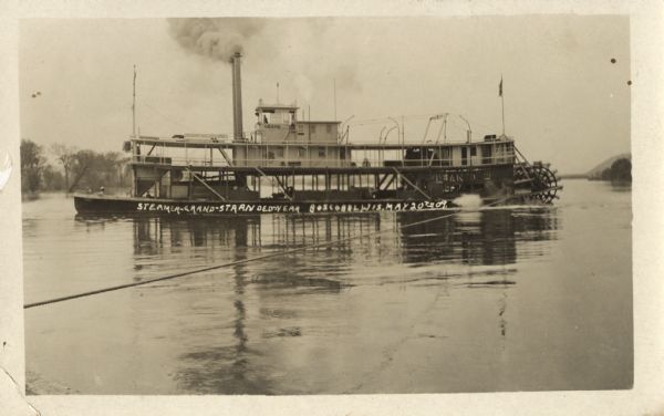 Photographic postcard of a paddle steamer on the Wisconsin River near Boscobel. Written on the hull of the boat is the text: "Steamer-Grand-Stranded-Near-Boscobel, Wis. May 20th 09."
