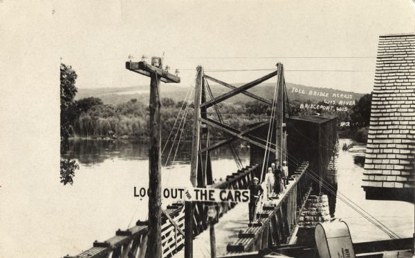 Photographic postcard of the toll bridge that spans the Wisconsin River. Part of the bridge is covered. Several men stand along the railing. A sign warns "Look Out for the Cars." Caption reads: "Toll Bridge Across Wis. River, Bridgeport, Wis."
