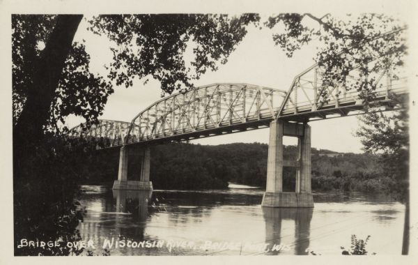 Photographic postcard view from shoreline towards the bridge over the Wisconsin River. Caption reads: "Bridge Over Wisconsin River, Bridgeport, Wis."