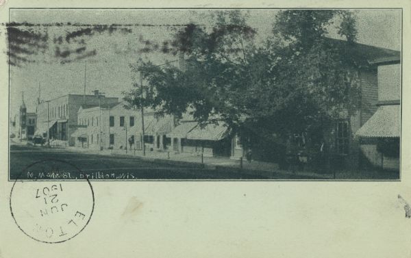 Postcard of North Main Street. Buildings line the right side of the street and there are several large trees along the sidewalk. Text below reads: "N. Main St., Brillion, Wis."