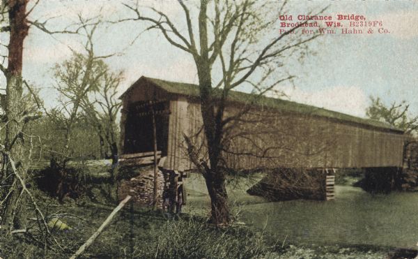 Colorized postcard view of the Old Clarance Bridge, a covered bridge. Text in red in the upper right corner reads: "Old Clarance Bridge, Brodhead, Wis."