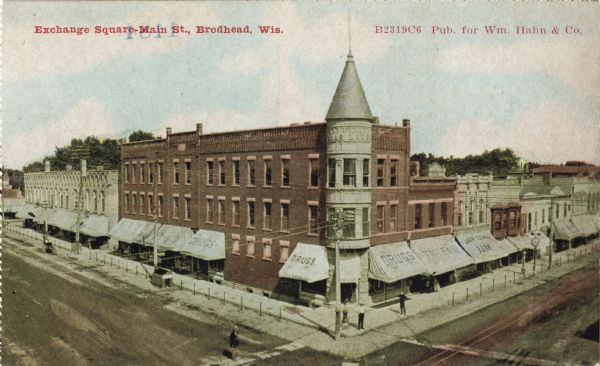 Colorized postcard of Exchange Square on Main Street. The elevated view shows a drug store on the corner and a bank to the right. Most buildings have awnings. Red text in the upper left reads: "Exchange Square, Main Street, Brodhead, Wis."