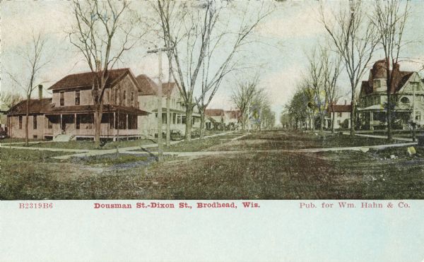 Colorized postcard view of the Dousman Street-Dixon Street intersection. The neighborhood has residential homes, sidewalks, and trees. Caption reads: "Dousman St.-Dixon St. Intersection, Brodhead, Wis."