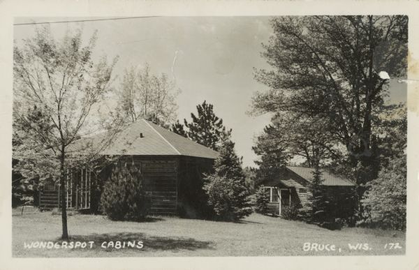 Photographic postcard view of two cabins surrounded by a lawn and trees at the Wonderspot Resort. Caption reads: "Wonderspot Cabins, Bruce, Wis."