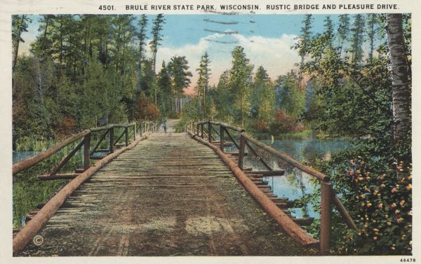 Colorized postcard of a wooden bridge over the Brule River flowing through the forest. A person is on the far side of the bridge. Caption reads: "Brule River State Park, Wisconsin. Rustic Bridge and Pleasure Drive."