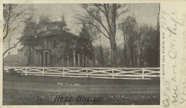 Black and white postcard of Hull House. The house was built in the Italianate style around 1850. Farm outbuildings are in the background. The house was still standing in 2006. Text at foot reads: "Hull House" and on the right "Butte Des Morts, Wis."