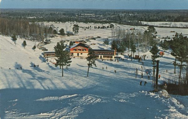 Color postcard of an elevated view of the Chalet at Mt. Telemark and surrounding area, and many skiers and several ski lifts.
