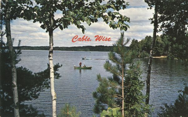 Color postcard of a view of a lake from a shoreline. A power boat and a fishing boat can be seen through the trees. "Cable, Wisc." is printed in red on the front using letterpress.