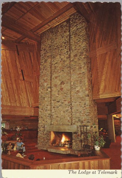 Color postcard of the interior of the Lodge at Telemark showing one of the largest stone fireplaces in the world. It is constructed out of 155 tons of native stone towering 55 feet high. Caption reads: "The Lodge at Telemark."