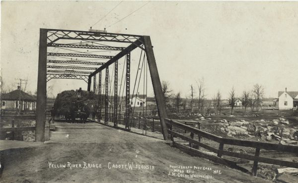 Photographic postcard of the Yellow River Bridge. A horse-drawn wagon full of hay is crossing the bridge. Houses and trees can be seen on the far side of the river.