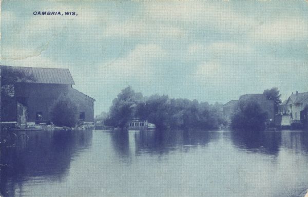 Colorized postcard of Tarrant Lake with buildings along the shoreline. Caption reads: "Cambria, Wis."