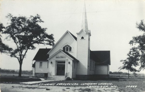Photographic postcard of St. James Evangelical Lutheran Church. Trees are on the left and right. Caption reads: "St. James Evangelical Lutheran Church, Cambridge, Wis."