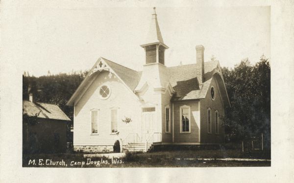 Photographic postcard of the Methodist Episcopal Church with trees in the background. Caption reads: "M.E. Church, Camp Douglas, Wis."