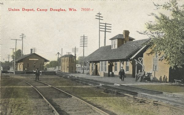 Colorized postcard of the Union Railroad depot. A railroad worker stands on the tracks, one man walks on the platform with his baggage and two men sit on a bench. Many electrical, telephone or telegraph poles are visible. Text in red in upper left corner: "Union Depot, Camp Douglas, Wis."