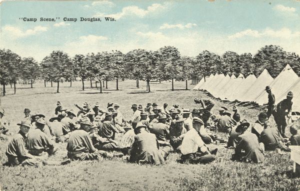 Colorized postcard of a camp scene with a group of soldiers. Most are seated on the grass in the foreground and many are in uniform. A row of tents are on the right and a grove of trees is visible in the background. Text in the upper left corner: "'Camp Scene,' Camp Douglas, Wis."