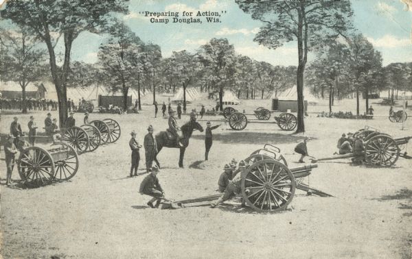 Colorized postcard of a combat drill. The scene includes soldiers, horses, wagons, cannons, tents, buildings and trees. Text above reads: "'Preparing for Action,' Camp Douglas, Wis."