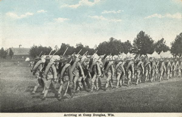 A colorized postcard of soldiers in uniform arriving at camp, marching in a column. They have bedrolls and weapons over their shoulders. Trees and tents are in the background, and a barn is on the left. Text at the foot reads: "Arriving at Camp Douglas, Wis."