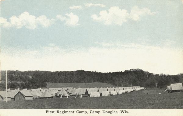 Colorized postcard of the First Regiment Camp. Many tents are pitched in rows and a few soldiers stand nearby. Bluffs and trees are in the background. Caption reads: "First Regiment Camp, Camp Douglas, Wis."