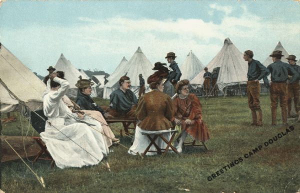 Colorized postcard of a group of women visiting soldiers in a camp. They are sitting on folding chairs next to a tent. One soldier is sitting with the women, and other men are standing behind and to the right. Many tents are pitched around them. Printed diagonally across the lower right corner: "Greetings Camp Douglas."