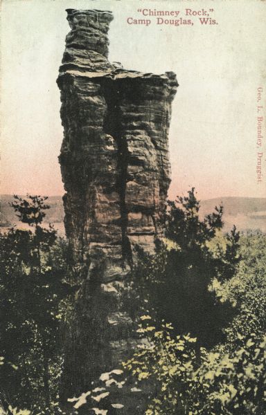 Colorized postcard of Chimney Rock. Trees surround the base. Text at top: "'Chimney Rock,' Camp Douglas, Wis."