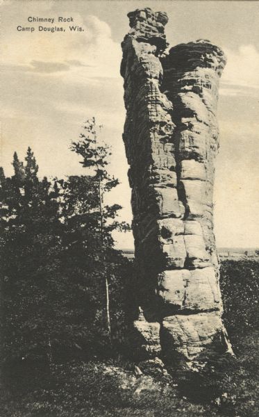 Black and white postcard of Chimney Rock. Trees surround the base. Text at top: "Chimney Rock, Camp Douglas, Wis."