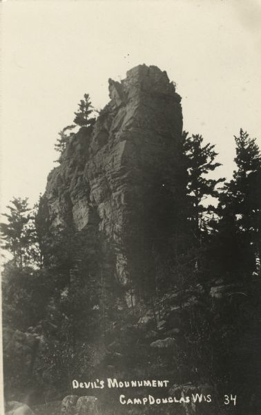Photographic postcard of Devil's Monument with trees surrounding it. Text handwritten at foot: "Devil's Monument, Camp Douglas, Wis. 34."