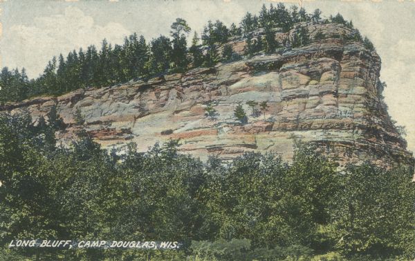 Colorized postcard of Long Bluff. Trees are growing on top of the bluff and also below. Text below reads: "Long Bluff, Camp Douglas, Wis."