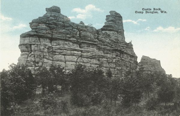 Colorized postcard of Castle Rock with trees all around the base. Text in upper right corner reads: "Castle Rock, Camp Douglas, Wis."