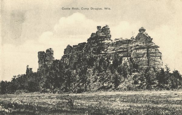 Black and white postcard of Castle Rock with trees all around the base. Text above reads: "Castle Rock, Camp Douglas, Wis."