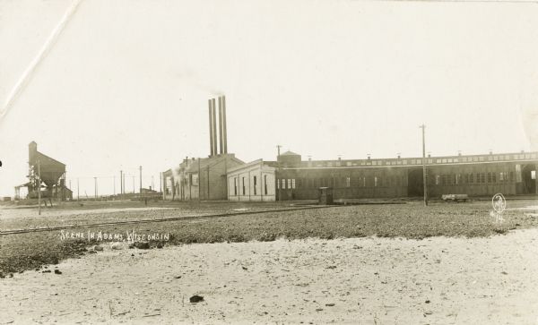 Photographic postcard of railroad yards. View of railroad tracks and buildings in the distance. A coal tipple is visible in the far left background.