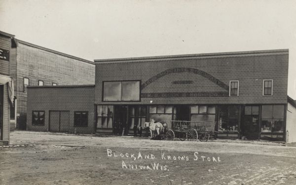 Photographic postcard of the Aniwa Mercantile Company building (1903), housing Block and Krom's Store. A horse-drawn cart is parked in front of the store and two children stand nearby. Merchandise is visible through the ground floor windows. Caption reads: "Block and Krom's Store, Aniwa, Wis."