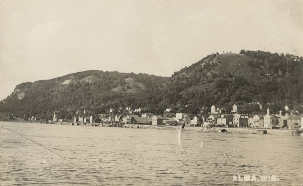 Photographic postcard view of Alma looking north. The Mississippi River is in the foreground. Caption reads: "Alma, Wis."