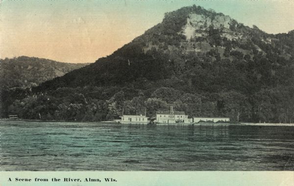 Colorized postcard of the Mississippi River and bluffs near Alma. A docked paddle boat is near the shoreline. Caption reads: "A Scene from the River, Alma, Wis."