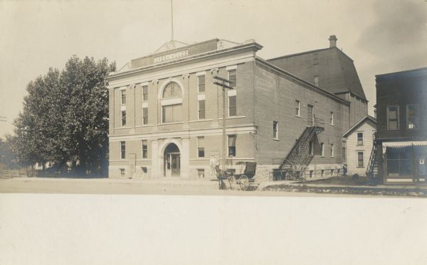 Photographic postcard view across street toward the three-story, brick opera house. A horse-drawn carriage is on the street in front.