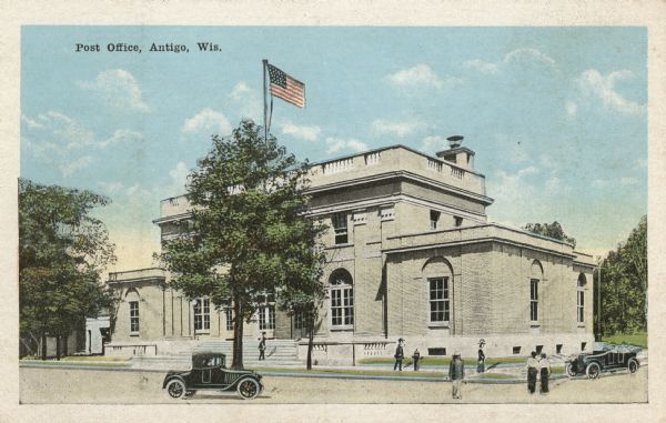 Color postcard view of the front of the old Post Office. Scene shows the front exterior of the building with flagstaff, a car driving down the street and pedestrians on the sidewalk. Caption reads: "Post Office, Antigo, Wis."