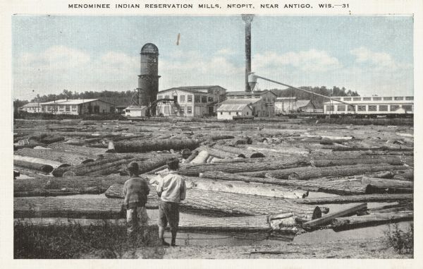 Mill on the Menominee Indian Reservation between Antigo and Shawano. Two young boys are standing in the foreground on the shoreline looking at logs ready for milling in Neopit. The mill is in the background. Caption reads: "Menominee Indian Reservation Mills, Neopit, Near Antigo, Wis."