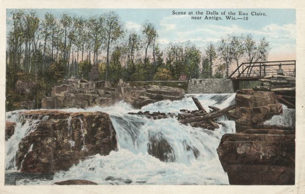 View looking up toward the falls and bridge at the Dells of Eau Claire. Caption reads: "Scene at the Dells of Eau Claire, near Antigo, Wis."