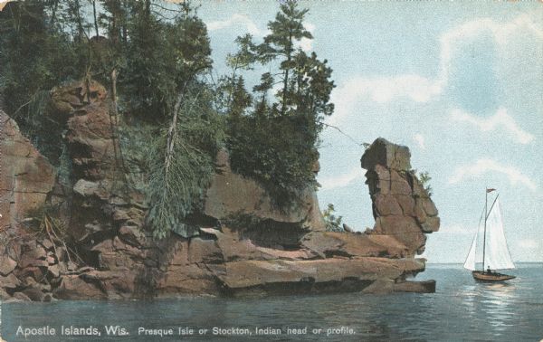 Postcard of the "Indian Head," or profile, a geological rock formation on the shorelinr. Caption reads: "Apostle Islands, Wis. Presque Isle or Stockton, Indian head or profile." A sailboat is near the shoreline on the right.