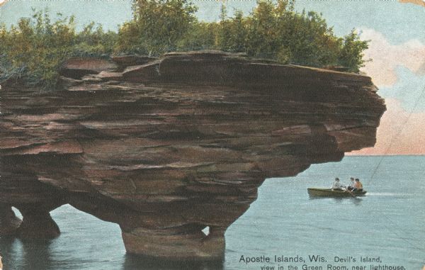 Colorized postcard of a view of the geologic formation known as the Green Room near the lighthouse on Devil's Island, part of the Apostle Islands. A boat with three passengers is on the right. Caption reads: "Apostle Islands, Wis. Devil's Island, view in the Green Room, near lighthouse."