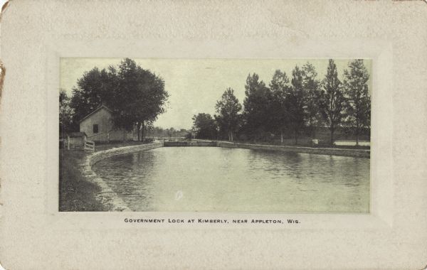Postcard of the government lock along the Fox River in Kimberly. A house and fence are along the shoreline to the left. Caption reads: "Government Lock at Kimberly, Near Appleton, Wis."