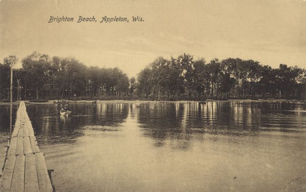 Scene at Brighton Beach. View of the lake and shoreline from what appears to be a wooden walkway across the water. A  man is rowing a rowboat nearby. Boats and buildings are behind the trees on the shoreline. Caption reads: "Brighton Beach, Appleton, Wis."